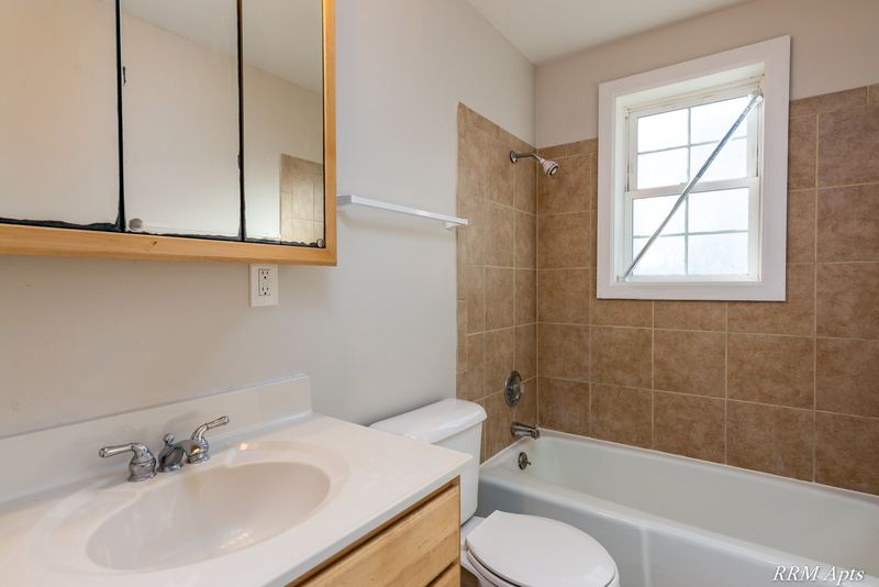 Bathroom with mirrored cabinet, white vanity, toilet and tan tile tub surround with window, Prairie Ridge apartment 9806 GA