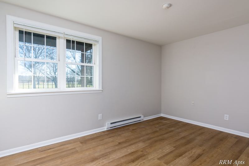 Empty room with wood floor, wide window on the left and a baseboard heater, Prairie Ridge apartment 9806 GA