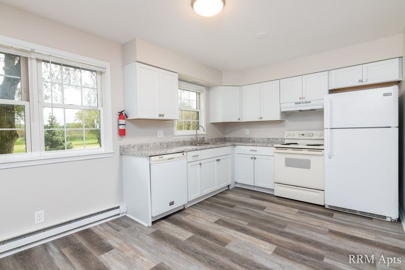 Kitchen with white cabinets, white refrigerator, stove and dishwasher, gray wood-look floor, Prairie Ridge apartment 9808-1D