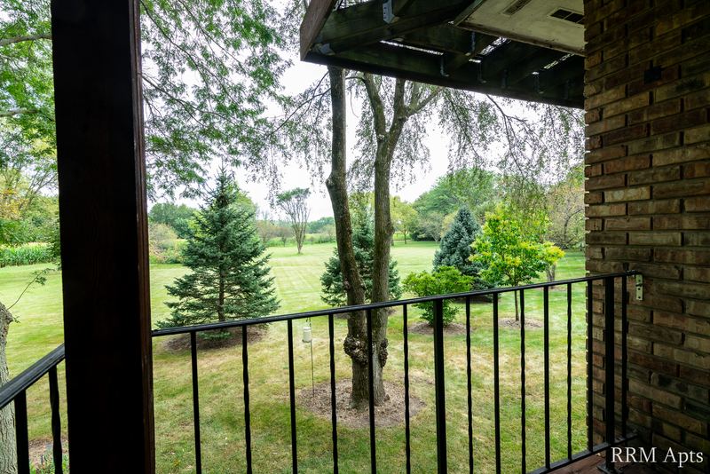 Balcony with black railing, brick column and a view of trees and lawn, Prairie Ridge apartment 9808-1D