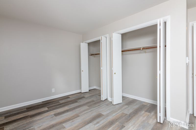 Bedroom with gray wood-look floor and two open closets with folding doors, Prairie Ridge apartment 9808-1D