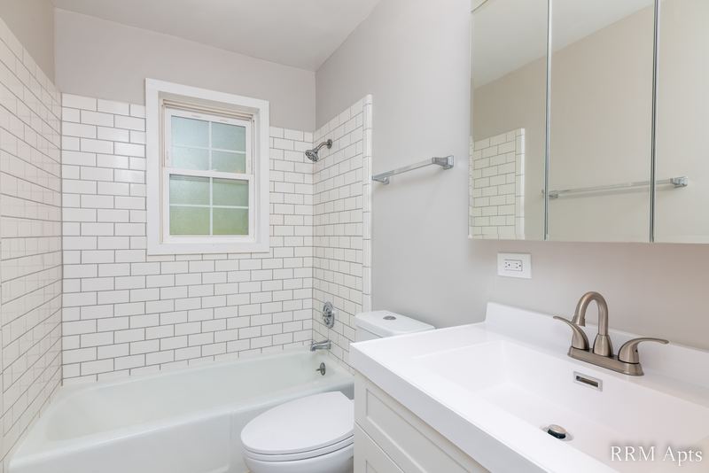 Bathroom with white subway tile tub surround, window, toilet and white vanity with mirror, Prairie Ridge apartment 9808-1D