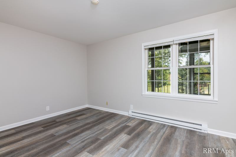 Empty room with gray wood-look floor, window on the right and a baseboard heater, Prairie Ridge apartment 9808-1D