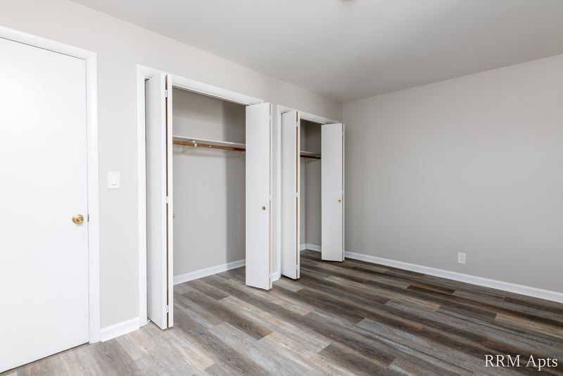 Bedroom with gray wood-look floor, white door and two open closets with rods, Prairie Ridge apartment 9808-1D