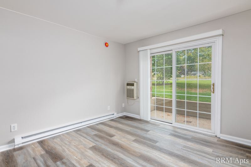 Living room with gray wood-look floor, sliding glass door and a wall air conditioner, Prairie Ridge apartment 9810 GB