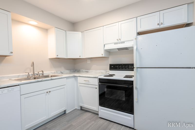 Kitchen with white cabinets, white refrigerator, black stove under a range hood and sink, Prairie Ridge apartment 9810 GB