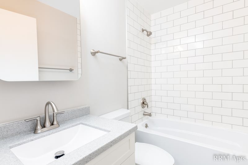 Bathroom with white vanity, gray counter, mirrored cabinet, toilet and subway tile tub, Prairie Ridge apartment 9810 GB