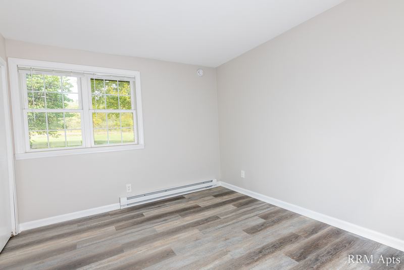 Empty room with gray wood-look floor, window onto trees and a baseboard heater, Prairie Ridge apartment 9810 GB