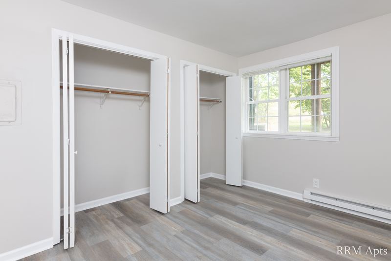 Bedroom with gray wood-look floor, window and two open closets with folding doors, Prairie Ridge apartment 9810 GB