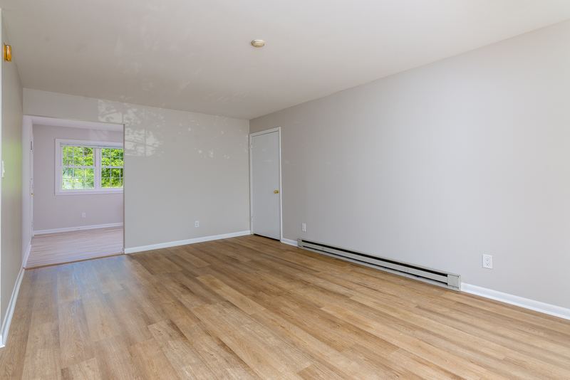 Living room with wood floor, baseboard heater and an opening to the hall and door, Prairie Ridge apartment 9812 1D