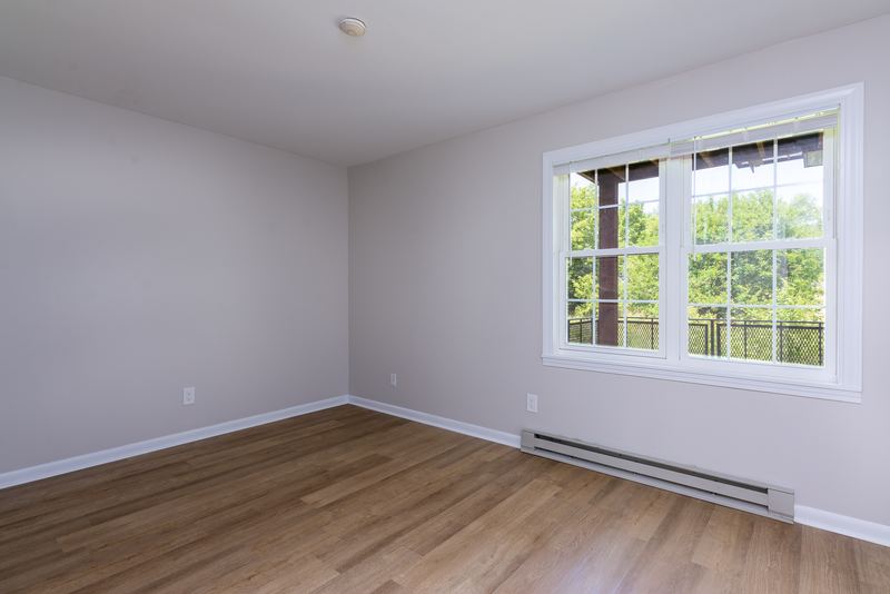 Empty room with wood floor, window with trees outside and a baseboard heater beneath it, Prairie Ridge apartment 9812 1D