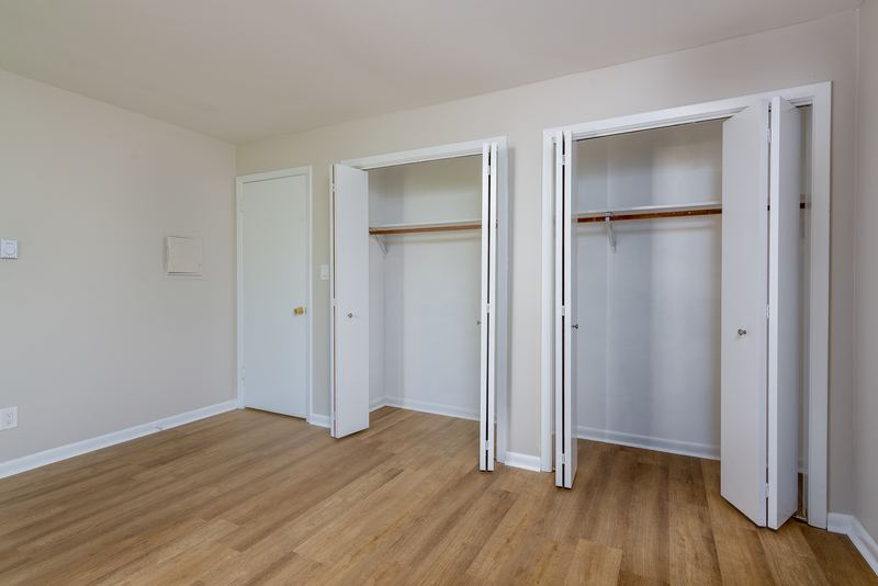 Bedroom with wood floor, white door on the left and two open closets with rods, Prairie Ridge apartment 9812 1D