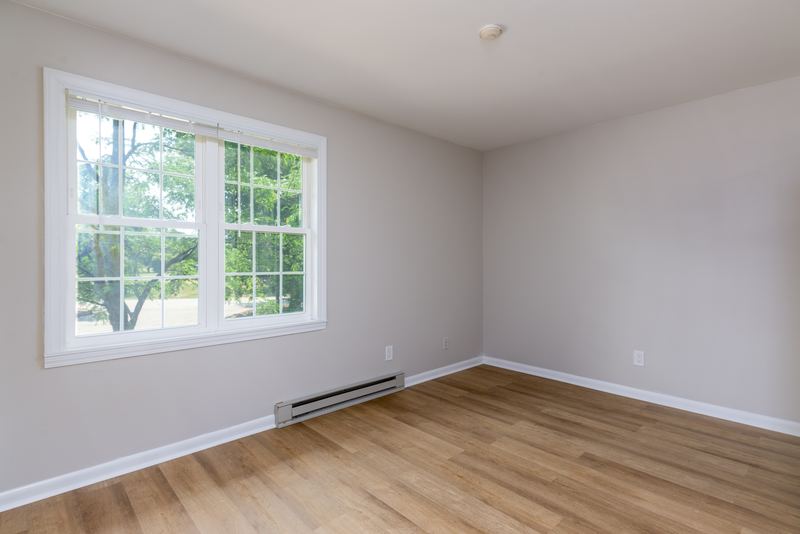 Empty room with wood floor, window on the left with trees outside and baseboard heater, Prairie Ridge apartment 9812 1D