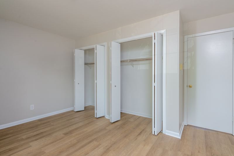 Bedroom with wood floor, open closet with folding doors and rod, and a white door, Prairie Ridge apartment 9812 1D