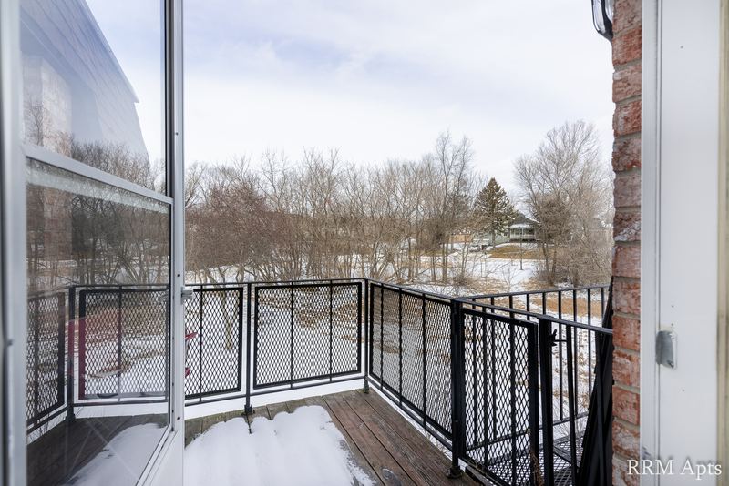Balcony with black railing, dusting of snow and a view of bare trees, brick column, Prairie Ridge apartment 9812 2D