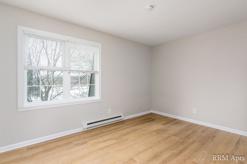 Empty room with wood floor, window onto trees and a baseboard heater below, Prairie Ridge apartment 9812 2D
