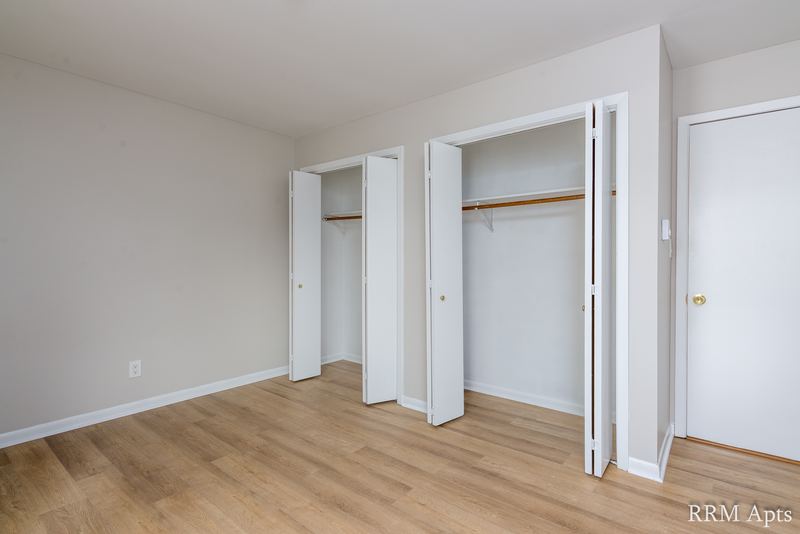 Bedroom with wood floor, two open closets with rods and a white door on the right, Prairie Ridge apartment 9812 2D