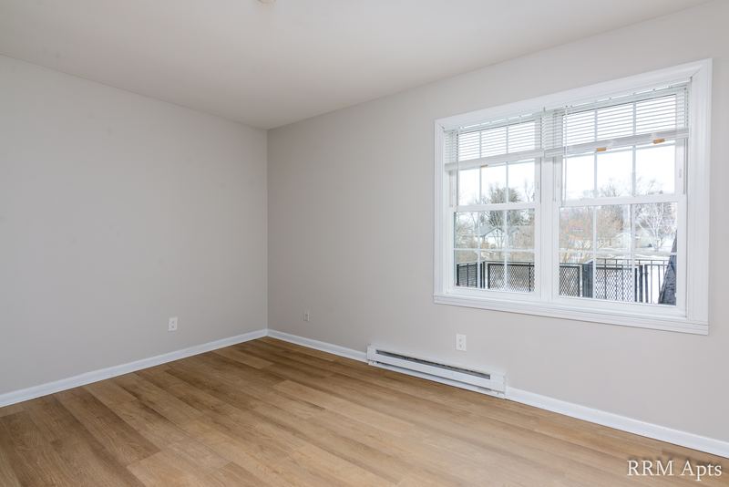 Empty room with wood floor, double window with trees outside and baseboard heater, Prairie Ridge apartment 9812 2D