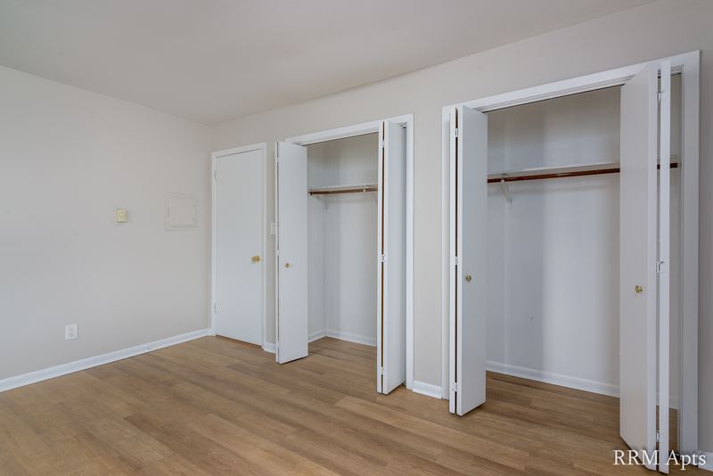 Bedroom with wood floor, door on the left and two open closets with folding doors, Prairie Ridge apartment 9812 2D