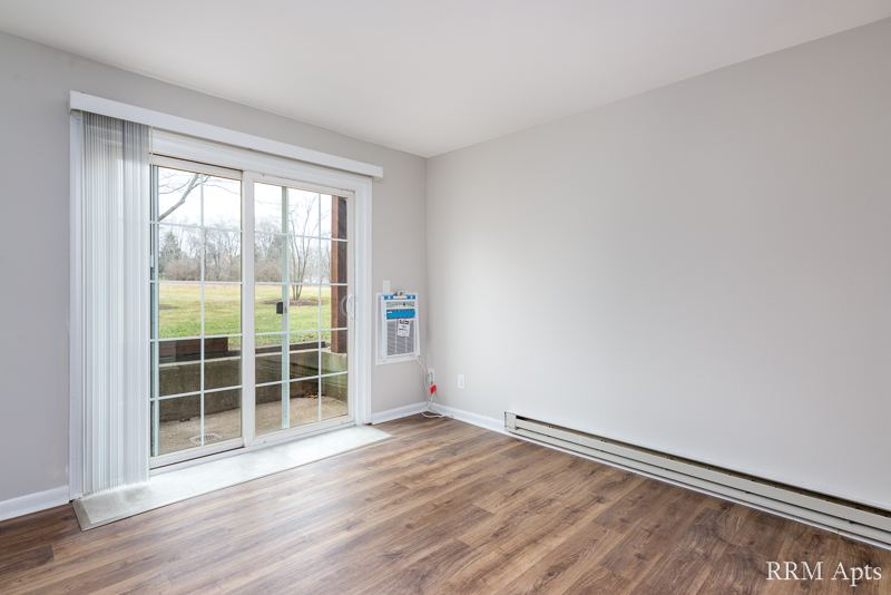 Living room with sliding glass door to a patio, wall air conditioner and wood-look floor, Prairie Ridge apartment GC