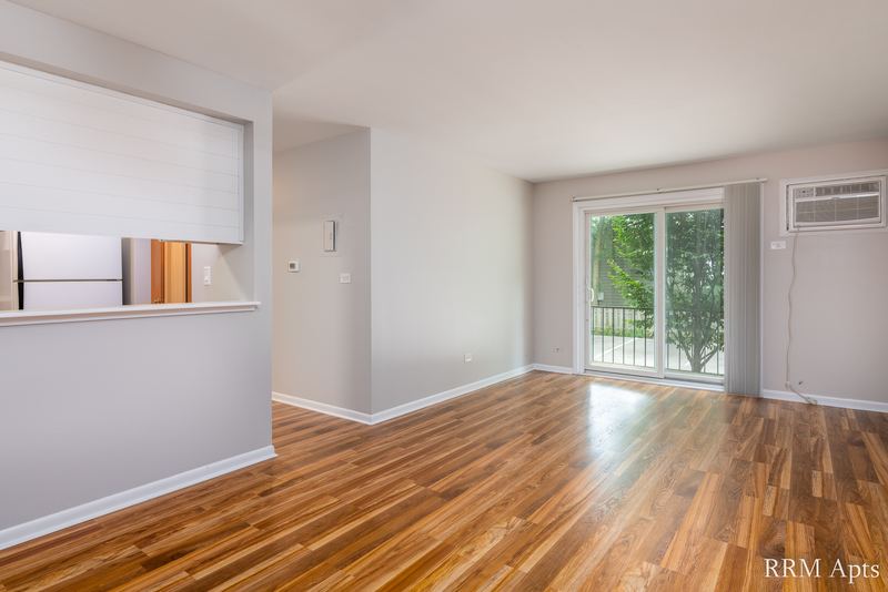 Living room with wood floor, sliding glass door onto trees and a wall air conditioner, Slusser Street apartment 1