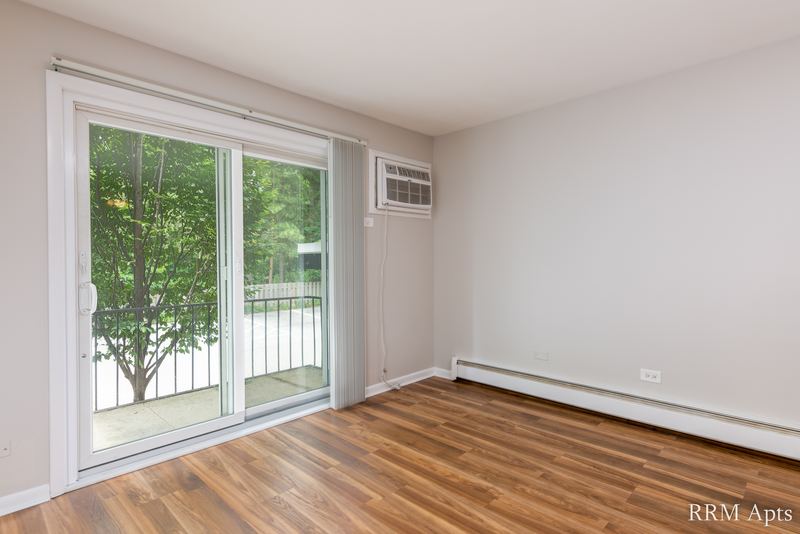 Living room with wood floor, sliding glass door, wall air conditioner and baseboard heater, Slusser Street apartment 1