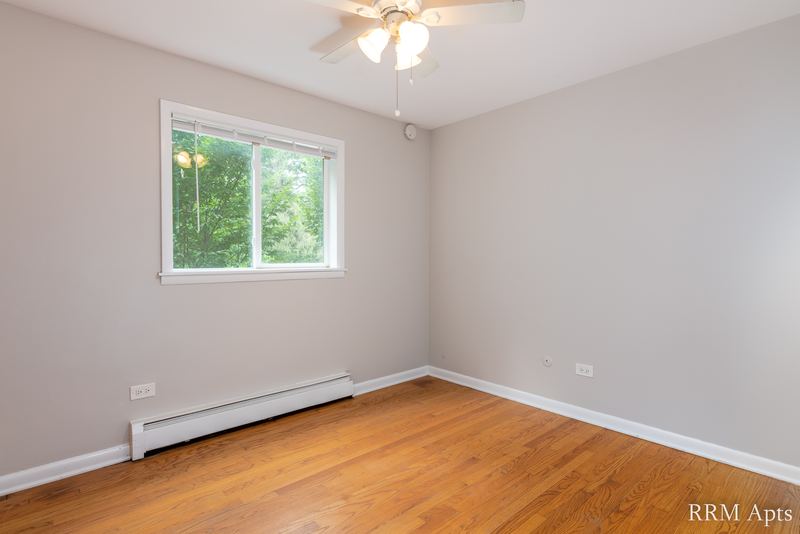 Empty room with wood floor, ceiling fan, window onto trees and a baseboard heater, Slusser Street apartment 1