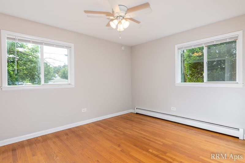 Empty room with wood floor, ceiling fan, two windows and a baseboard heater, Slusser Street apartment 1