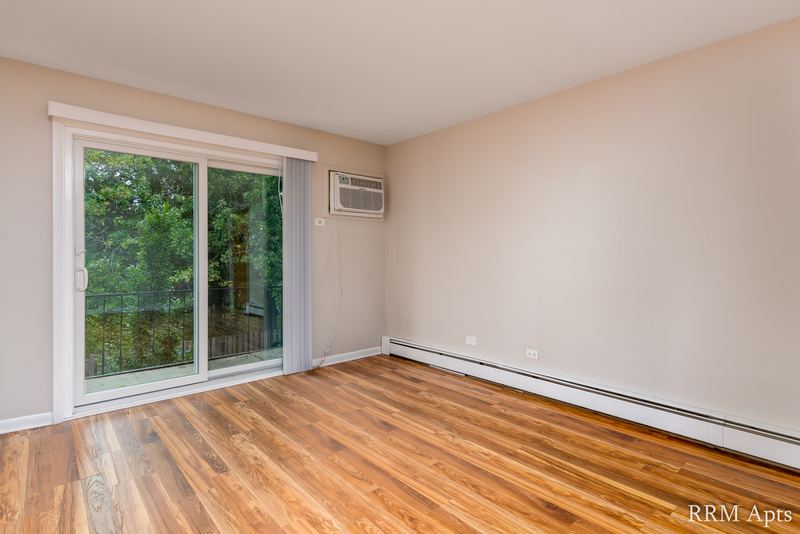 Living room with wood floor, sliding glass door with trees outside and a wall air conditioner, Slusser Street apartment 5