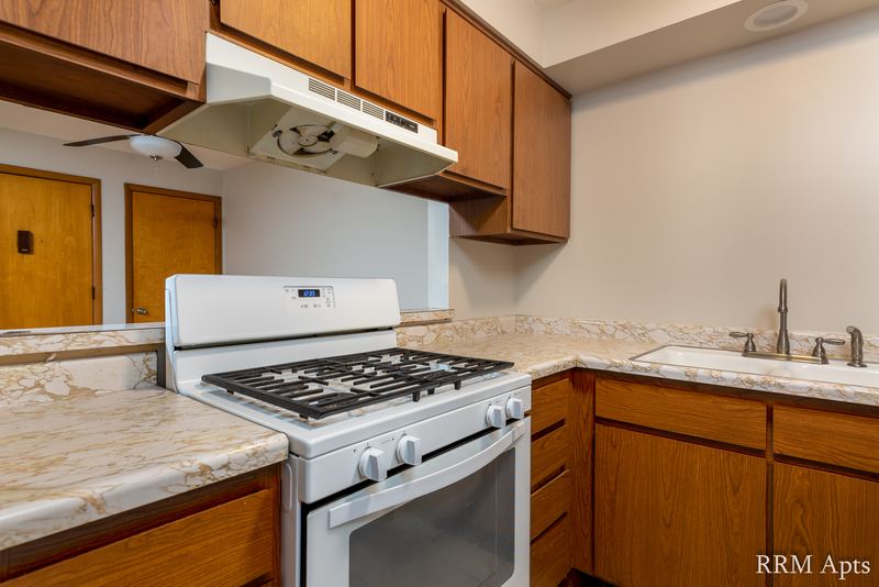 Kitchen with oak cabinets, white gas stove under a range hood and granite-look counter, Slusser Street apartment 5