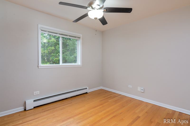 Empty room with wood floor, ceiling fan, window with trees and a baseboard heater, Slusser Street apartment 5
