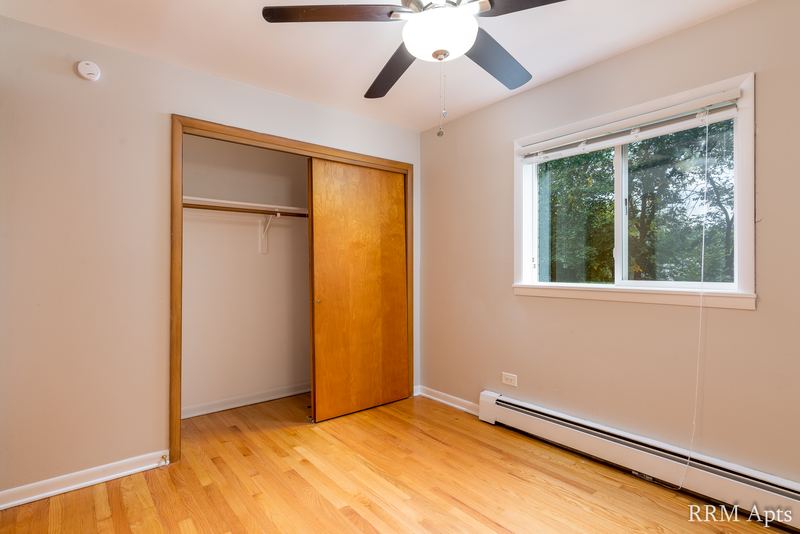 Bedroom with wood floor, ceiling fan, open closet with wood door and a window, Slusser Street apartment 5