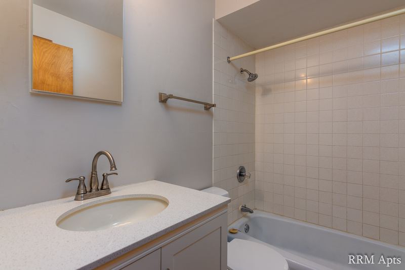 Bathroom with vanity, light counter, mirrored cabinet and white tile tub surround, Slusser Street apartment 5