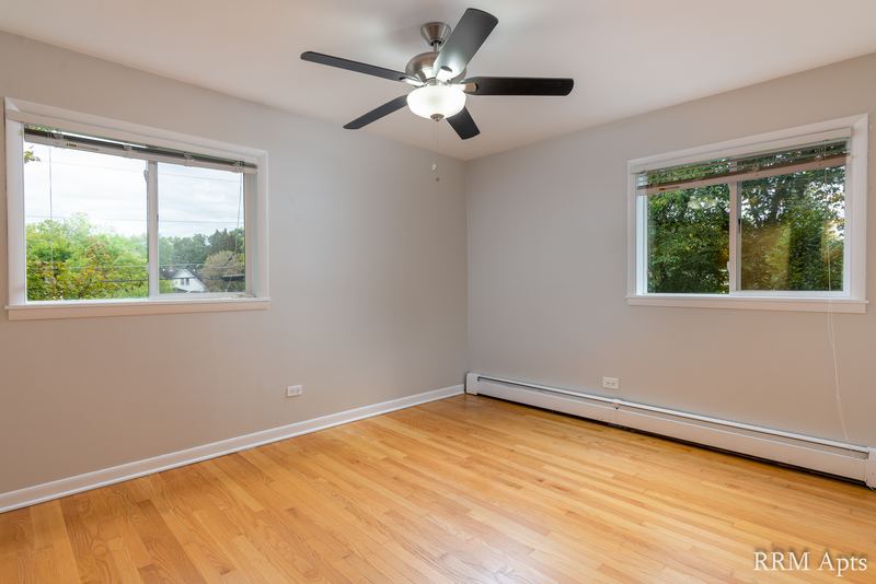 Empty room with wood floor, ceiling fan, two windows and baseboard heater along the wall, Slusser Street apartment 5