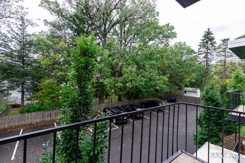 Balcony with black railing overlooking trees, a wood fence and parking area, Slusser Street apartment 5