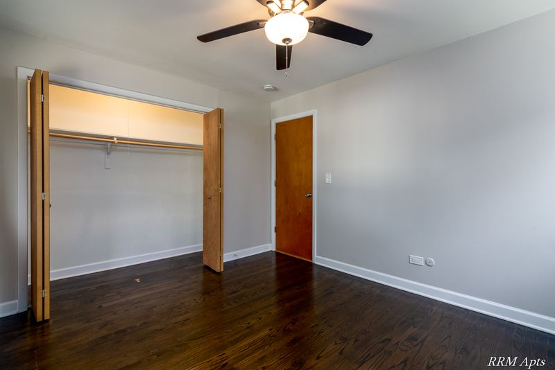 Bedroom with dark wood floor, ceiling fan, open bifold-door closet and wood entry door, Slusser Street apartment 7