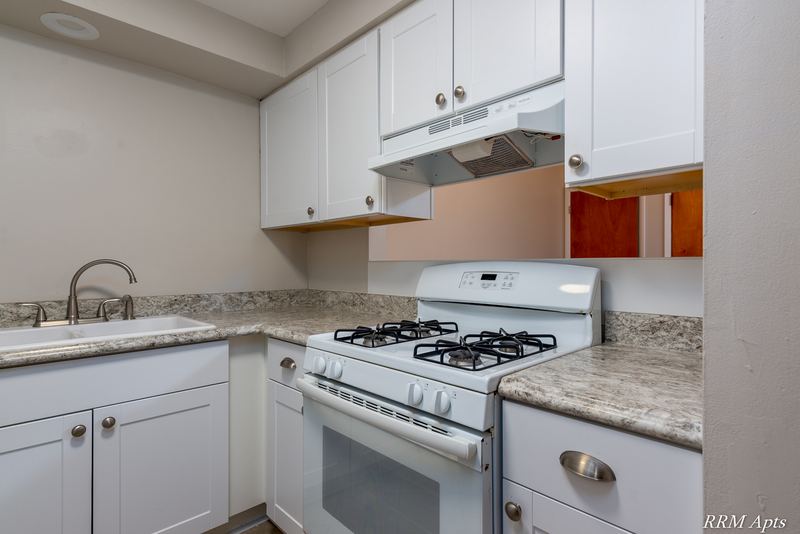 Kitchen with white cabinets, white gas stove under a range hood and granite-look counter, Slusser Street apartment 7