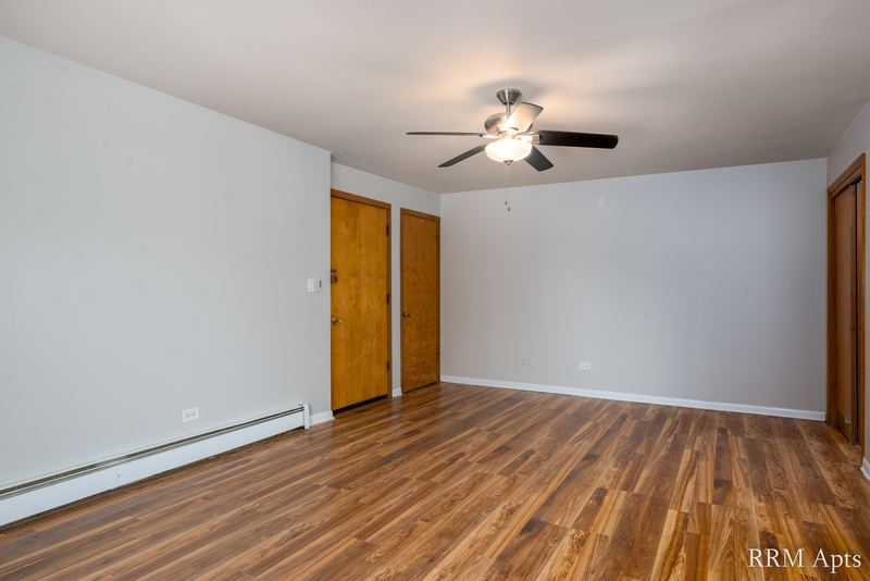 Living room with wood floor, ceiling fan, two wood doors and baseboard radiator, Slusser Street apartment 8