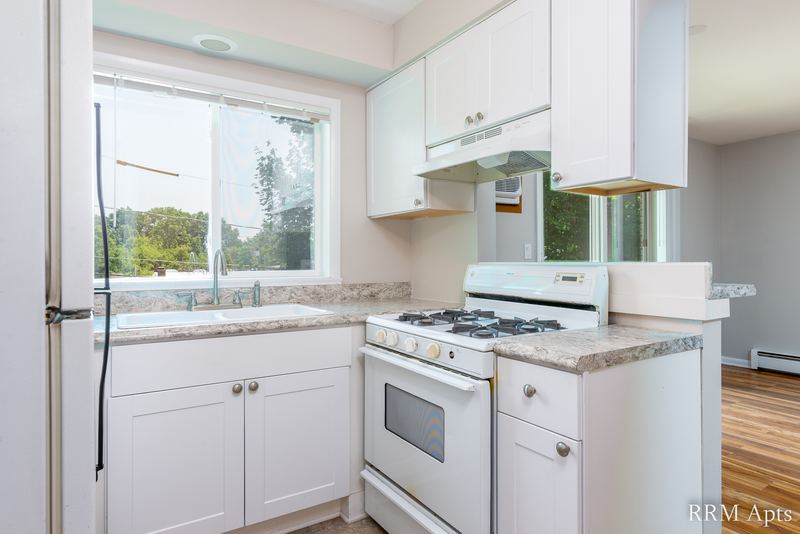 Kitchen with white cabinets, white gas stove, range hood, granite-look counter and wood floor, Slusser Street apartment 8