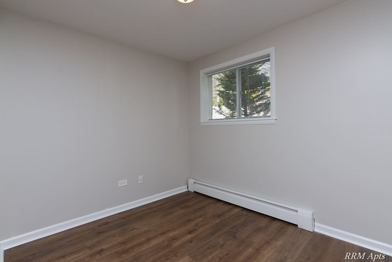 Bedroom with wood floor, single window facing trees and baseboard radiator, Slusser Street apartment 9