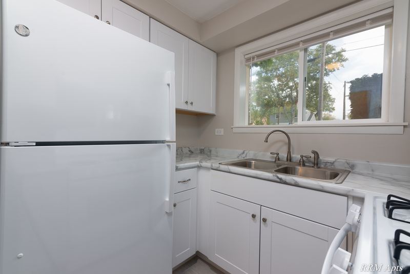 Kitchen with white cabinets, white refrigerator, marble-look counter and window over the sink, Slusser Street apartment 9