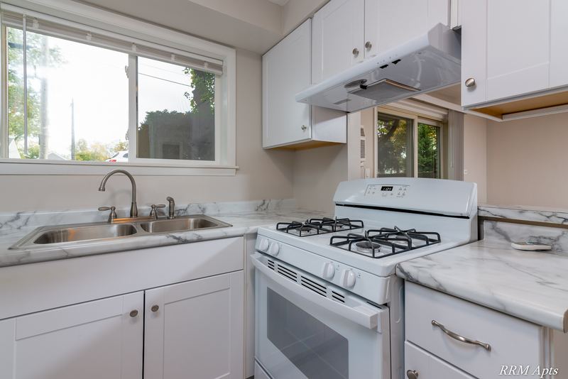 Kitchen with white cabinets, white gas stove, range hood and marble-look counter by the window, Slusser Street apartment 9