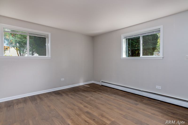 Bedroom with wood floor, two windows facing trees and baseboard radiator, Slusser Street apartment 9