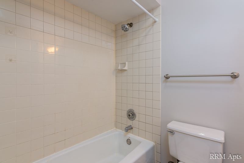 Bathroom with white tile tub surround, grab bar and toilet, South Slusser apartment 4