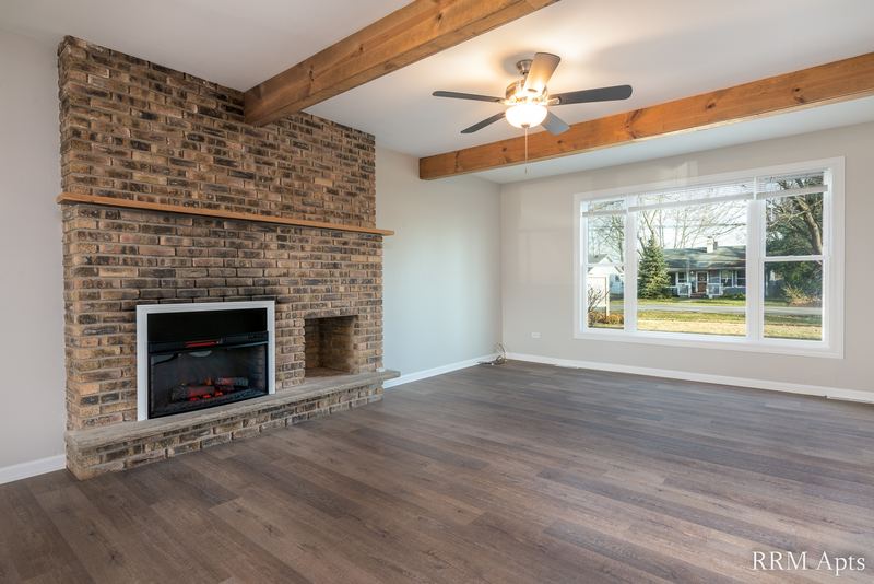 Living room with wood floor, brick fireplace, wood ceiling beam, ceiling fan and window, South Slusser apartment 430