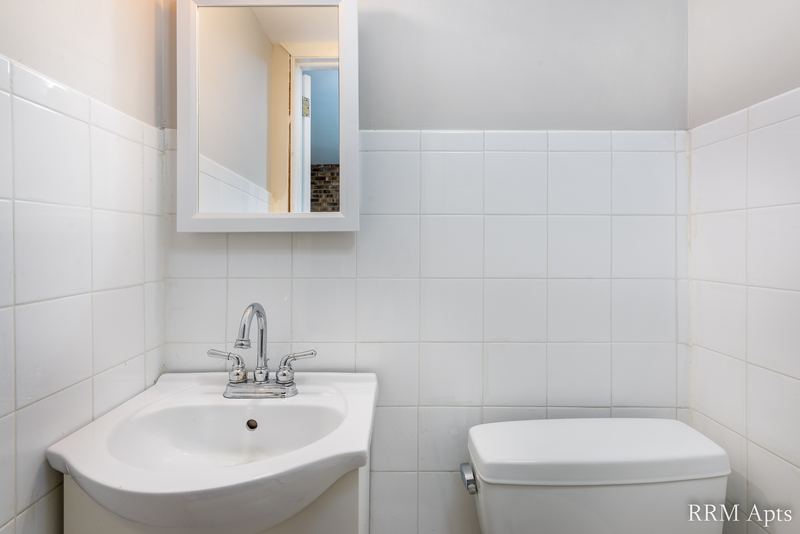 Bathroom with white tile walls, white pedestal sink, white toilet and medicine cabinet, South Slusser apartment 430