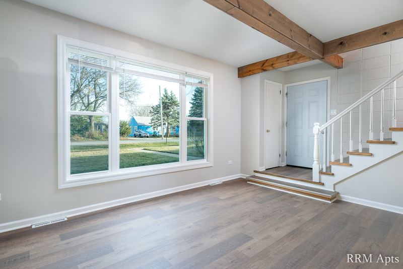Living room with wood floor, wide window, white entry door and white-railed staircase, South Slusser apartment 430
