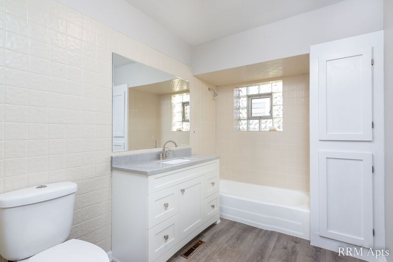 Bathroom with white vanity, glass block window, beige tile tub surround and white toilet, South Slusser apartment 430