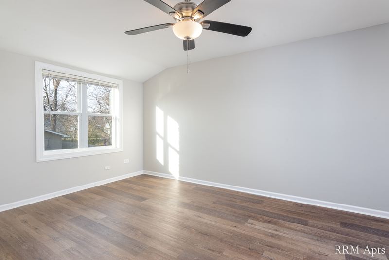Bedroom with wood floor, ceiling fan, sloped ceiling and window facing trees, South Slusser apartment 430