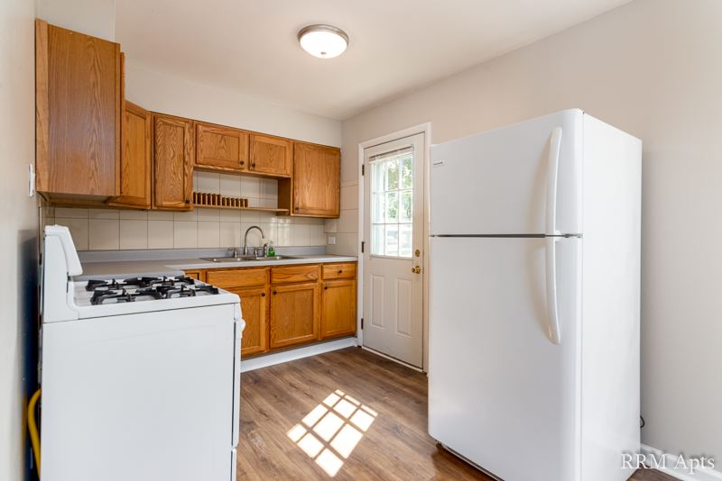 Kitchen with oak cabinets, white stove and refrigerator and a door to outside, South Slusser apartment 434